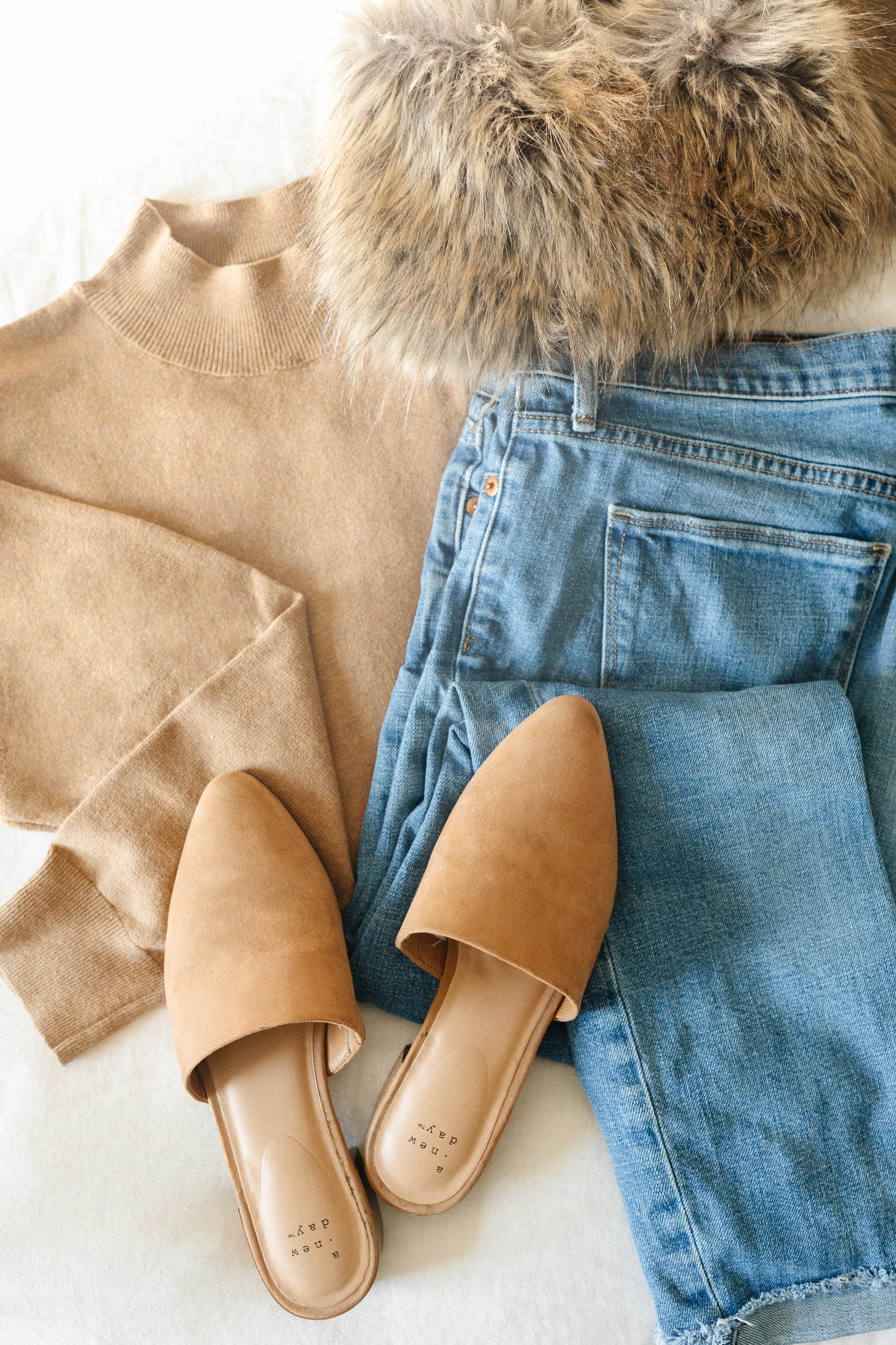 Winter outfit inspiration with brown sweater, blue jeans, fur scarf, and brown slip-on shoes.